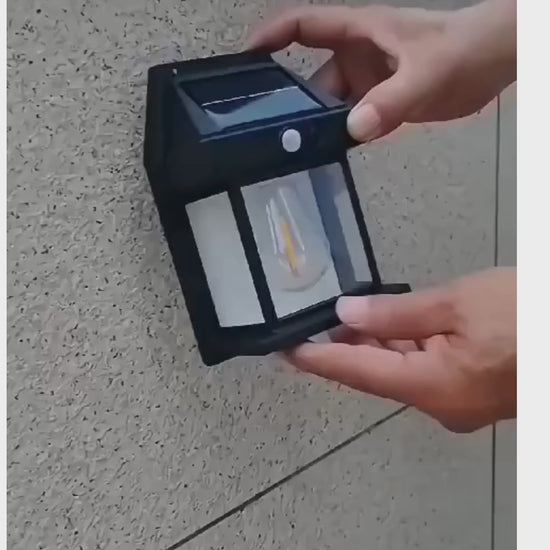Person installing a solar-powered outdoor light on a textured wall for eco-friendly illumination.