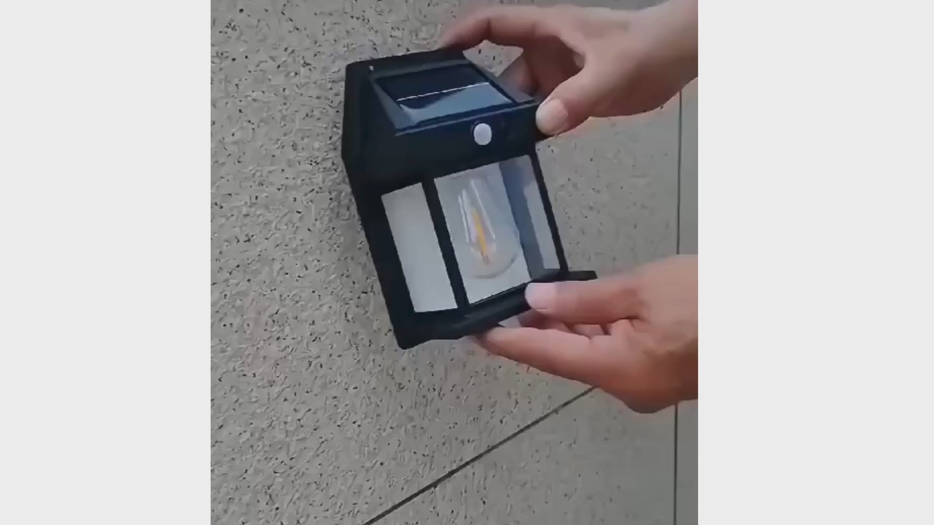 Person installing a solar-powered outdoor light on a textured wall for eco-friendly illumination.